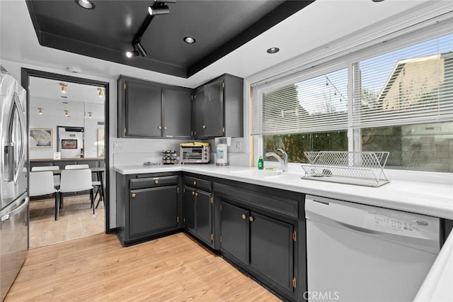 kitchen featuring white dishwasher, sink, light hardwood / wood-style flooring, and a raised ceiling