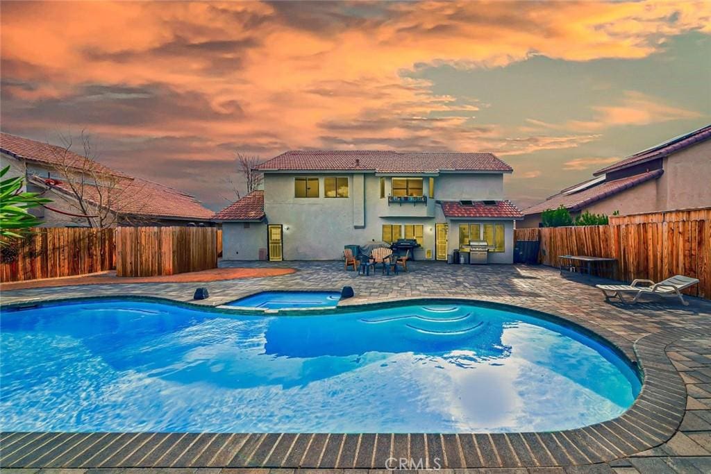 pool at dusk featuring a patio area and an in ground hot tub