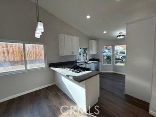 kitchen with vaulted ceiling, dark hardwood / wood-style floors, kitchen peninsula, hanging light fixtures, and white cabinets