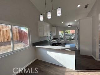 kitchen with lofted ceiling, kitchen peninsula, white cabinetry, hanging light fixtures, and dark hardwood / wood-style flooring