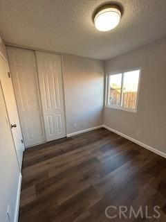 unfurnished bedroom featuring dark wood-type flooring, a textured ceiling, and a closet