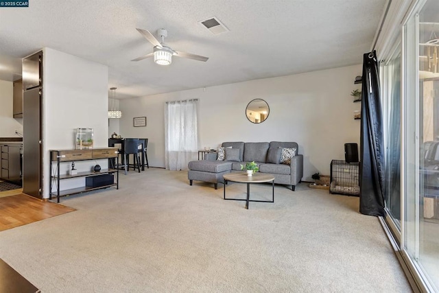 living room with ceiling fan, a textured ceiling, and light carpet