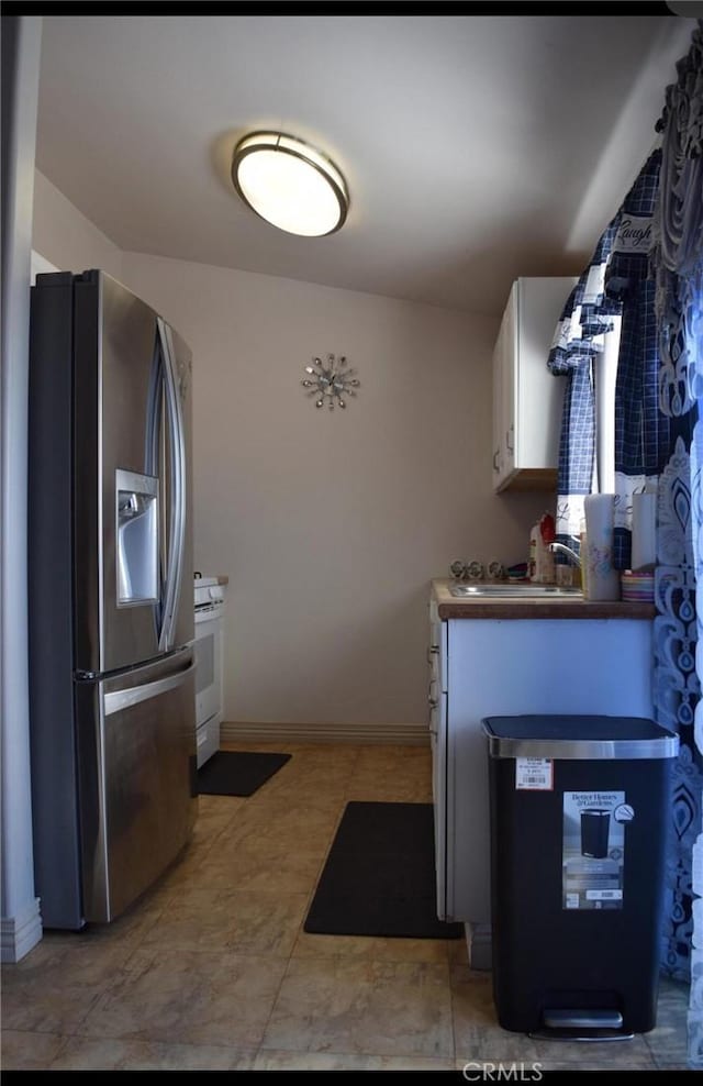 kitchen with white cabinets, stainless steel fridge, sink, and white range oven