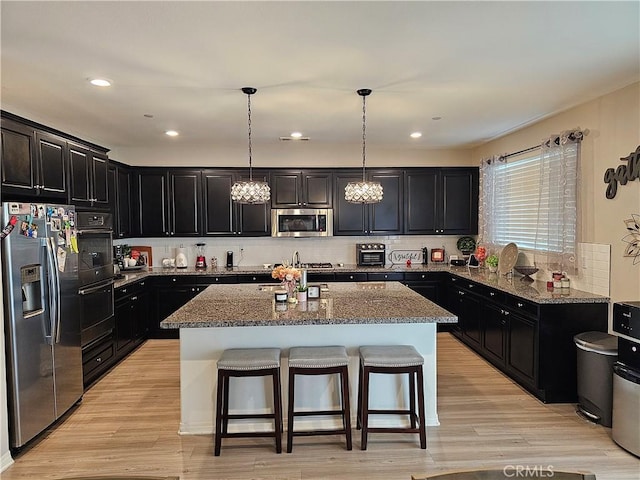 kitchen with appliances with stainless steel finishes, pendant lighting, stone countertops, and a kitchen island