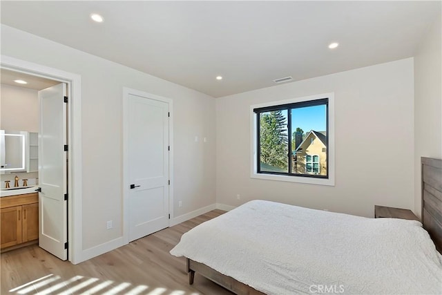 bedroom with light wood-type flooring, sink, and connected bathroom