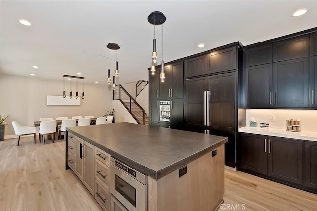 kitchen featuring hanging light fixtures, built in appliances, light hardwood / wood-style floors, and a center island