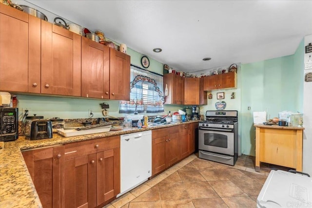 kitchen featuring stainless steel range with gas stovetop, dishwasher, light stone countertops, and light tile patterned floors