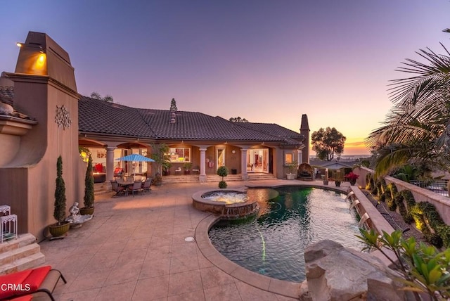 pool at dusk with pool water feature, a patio area, and an in ground hot tub