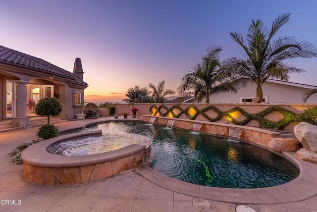 pool at dusk with pool water feature and an in ground hot tub