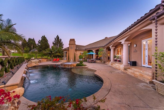 pool at dusk with pool water feature, french doors, a patio area, and an in ground hot tub