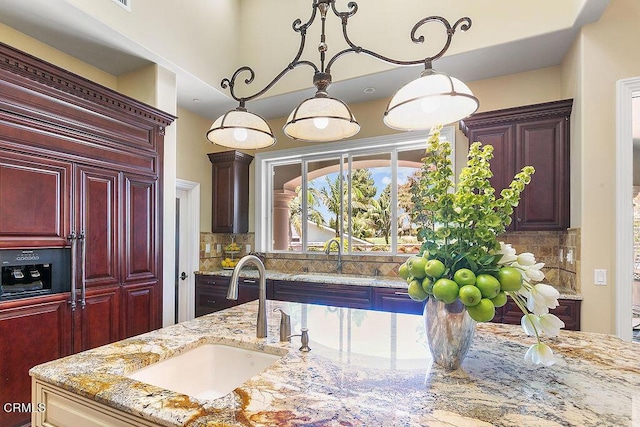 kitchen with decorative backsplash, sink, hanging light fixtures, and light stone countertops