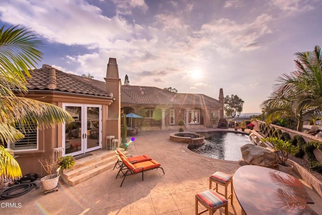 pool at dusk with french doors, a patio, and an in ground hot tub