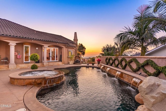 pool at dusk featuring pool water feature, french doors, and an in ground hot tub