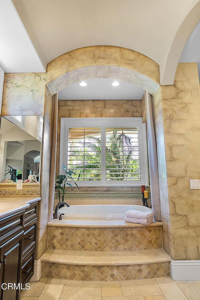 bathroom with vanity, a healthy amount of sunlight, and tiled tub