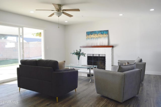 living room with a brick fireplace, dark hardwood / wood-style floors, and ceiling fan