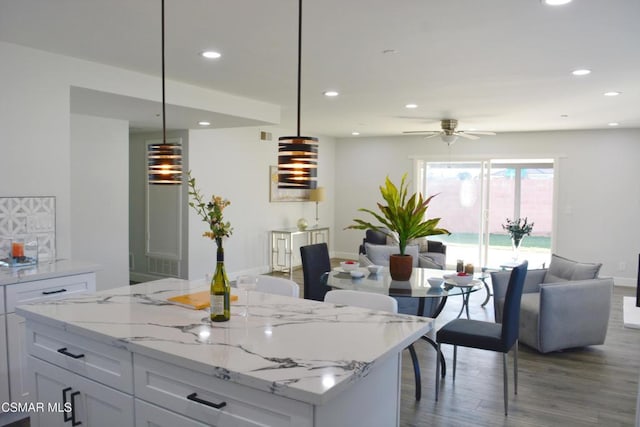 kitchen with decorative light fixtures, ceiling fan, wood-type flooring, white cabinetry, and light stone counters