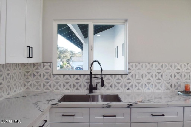 kitchen featuring decorative backsplash, light stone countertops, white cabinetry, and sink