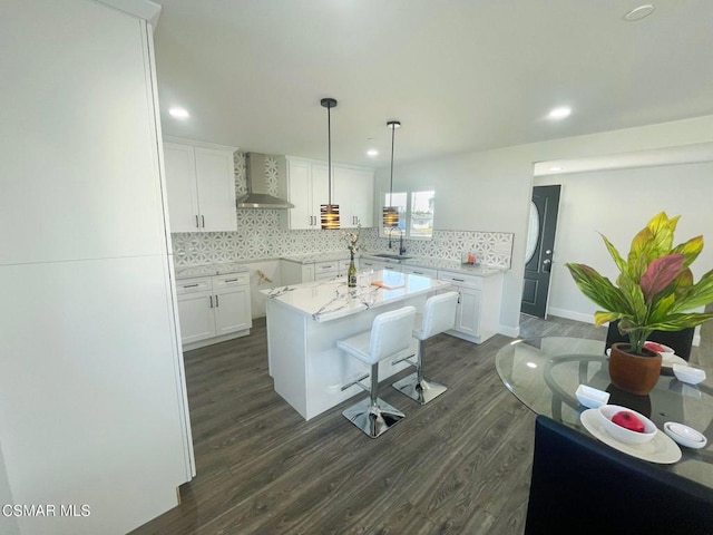 kitchen with dark hardwood / wood-style floors, wall chimney exhaust hood, white cabinets, and a center island with sink