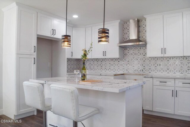 kitchen with a kitchen breakfast bar, pendant lighting, white cabinets, and wall chimney range hood