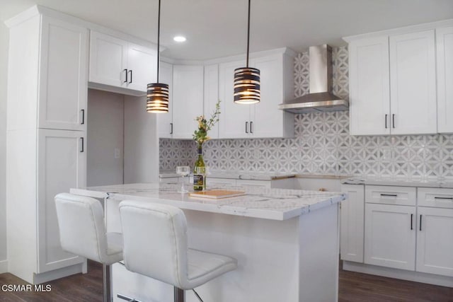 kitchen with white cabinetry, wall chimney exhaust hood, a kitchen bar, and decorative light fixtures