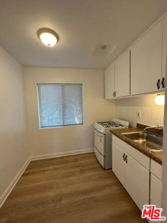 kitchen featuring dark wood-type flooring, white cabinets, white range with gas stovetop, and sink