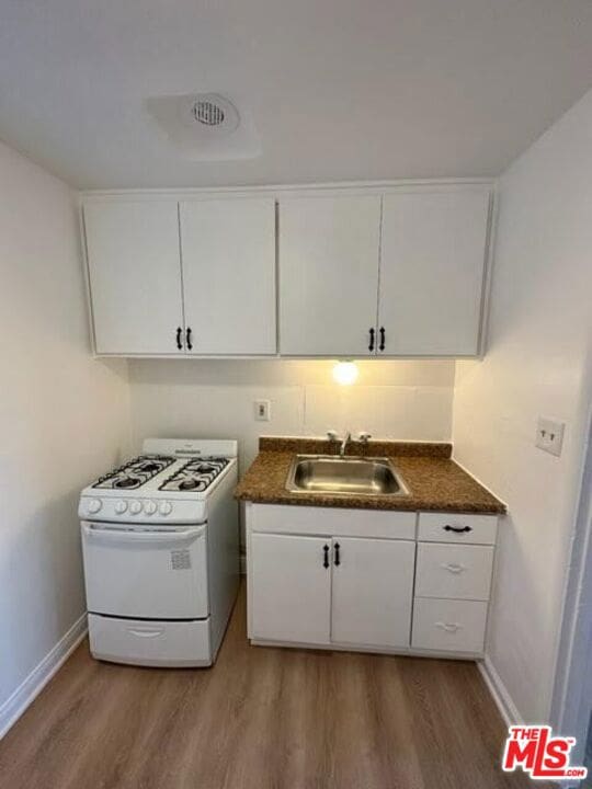 kitchen with hardwood / wood-style flooring, sink, white cabinets, and white gas stove