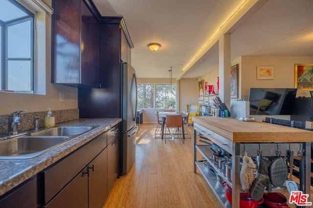 kitchen with sink, hanging light fixtures, dark brown cabinets, light hardwood / wood-style floors, and stainless steel refrigerator