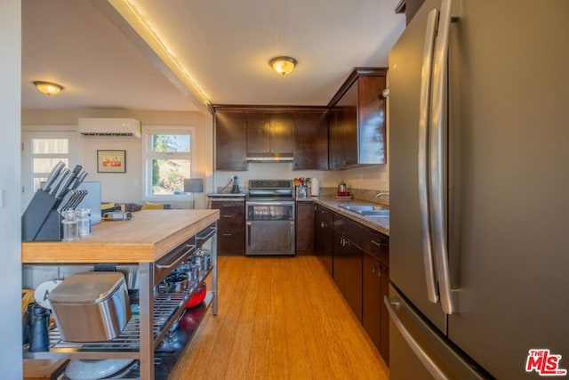 kitchen with a wall mounted air conditioner, appliances with stainless steel finishes, light wood-type flooring, dark brown cabinetry, and sink