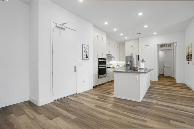 kitchen featuring light hardwood / wood-style floors, decorative backsplash, white cabinetry, a kitchen island with sink, and appliances with stainless steel finishes