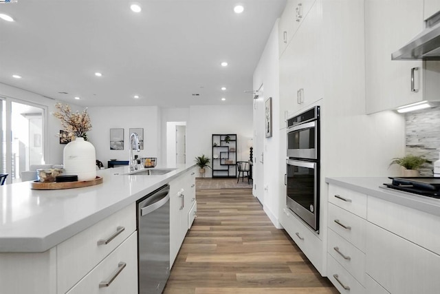 kitchen featuring white cabinetry, stainless steel appliances, sink, ventilation hood, and light hardwood / wood-style flooring