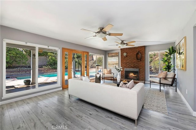 living room with a brick fireplace, a wealth of natural light, hardwood / wood-style floors, and ceiling fan