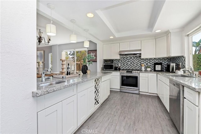 kitchen with light stone countertops, pendant lighting, appliances with stainless steel finishes, white cabinetry, and sink