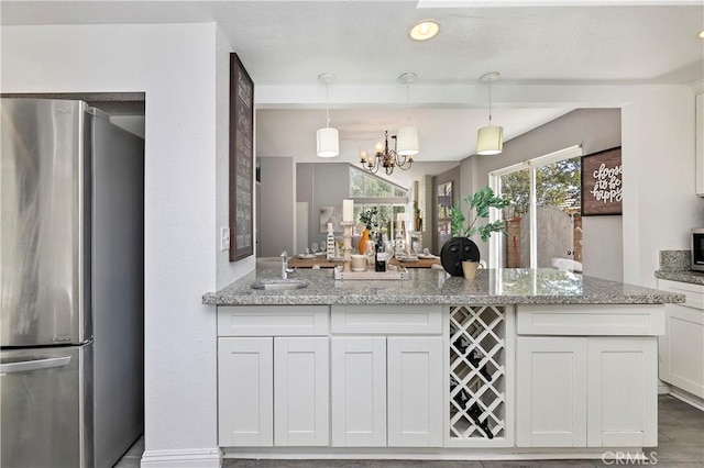 kitchen featuring light stone countertops, white cabinets, a chandelier, and stainless steel refrigerator