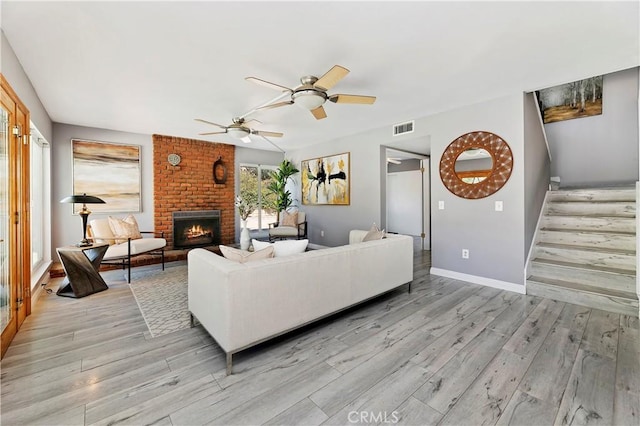 living room with ceiling fan, a brick fireplace, and light hardwood / wood-style flooring