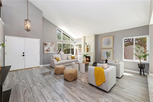 living room featuring light wood-type flooring, a fireplace, a notable chandelier, and high vaulted ceiling