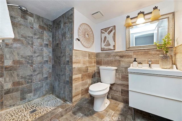 bathroom featuring a textured ceiling, vanity, tile walls, toilet, and tiled shower