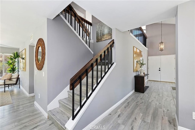 staircase with wood-type flooring, a towering ceiling, and a chandelier