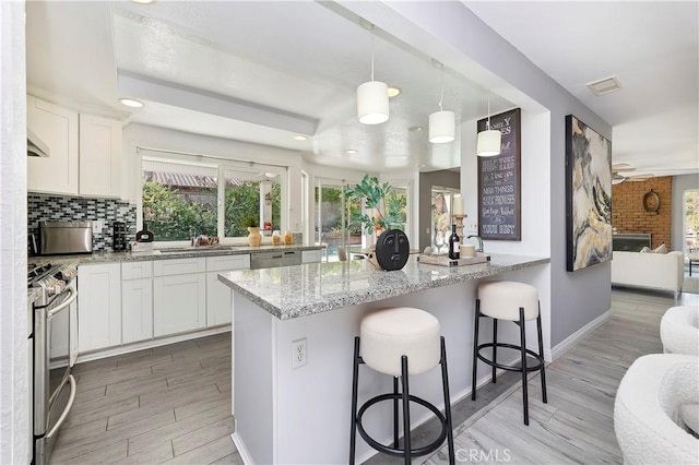 kitchen featuring a kitchen bar, appliances with stainless steel finishes, pendant lighting, white cabinets, and light stone counters