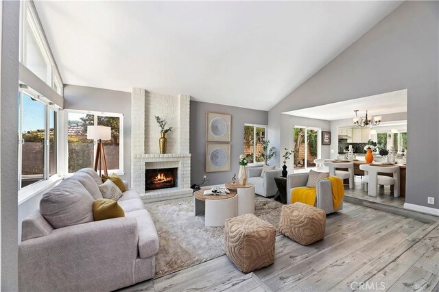 living room featuring a brick fireplace, a chandelier, lofted ceiling, and light hardwood / wood-style floors