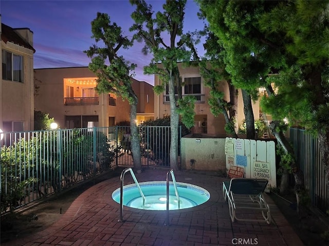 pool at dusk featuring a hot tub