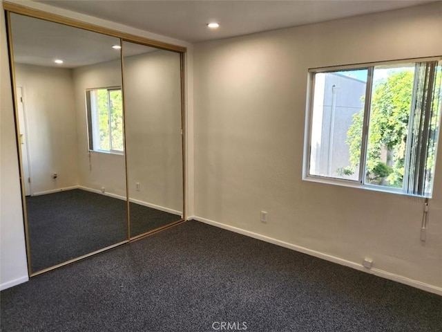 unfurnished bedroom with a closet, dark carpet, and multiple windows