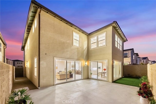 back of house at dusk featuring a patio area, a fenced backyard, and stucco siding