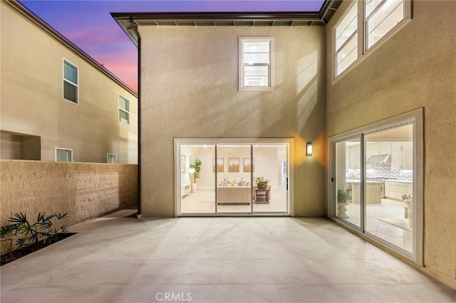 back of house at dusk with a patio area, fence, and stucco siding