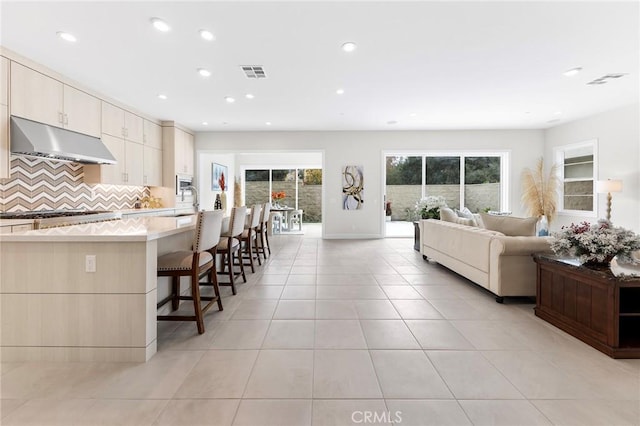 kitchen featuring visible vents, decorative backsplash, open floor plan, light tile patterned flooring, and under cabinet range hood