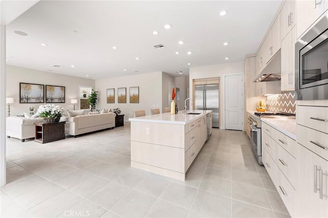 kitchen featuring a spacious island, decorative backsplash, sink, built in appliances, and light tile patterned floors