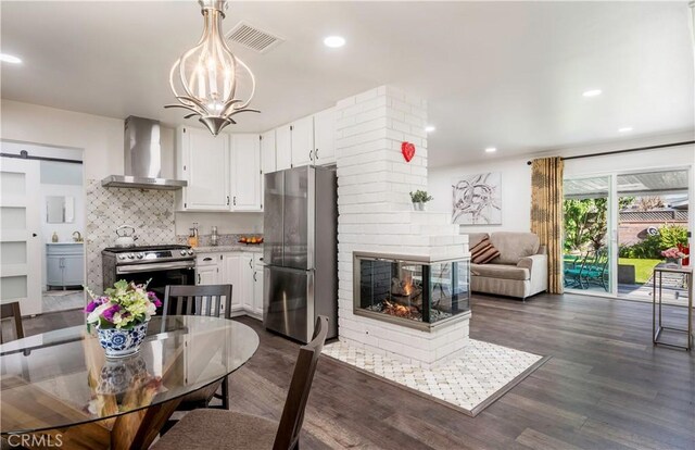 kitchen featuring stainless steel appliances, white cabinetry, wall chimney exhaust hood, a barn door, and pendant lighting