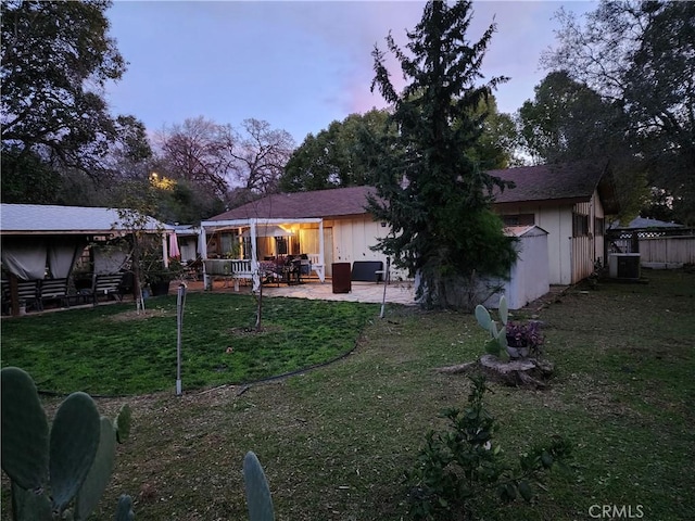 back house at dusk featuring central air condition unit, a yard, and a patio