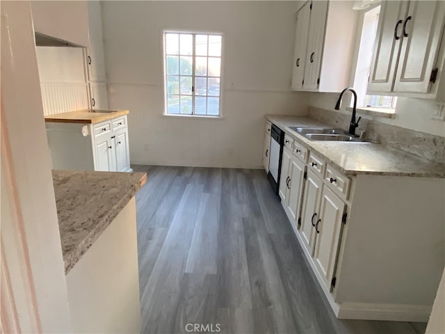 kitchen with dishwasher, sink, white cabinets, light stone counters, and dark wood-type flooring