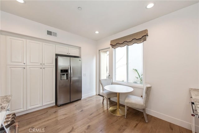 kitchen with stainless steel fridge with ice dispenser, white cabinetry, light hardwood / wood-style flooring, and light stone counters