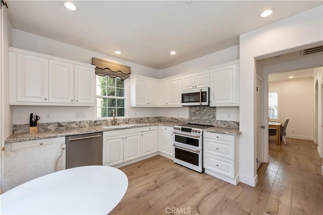 kitchen with white cabinets, tasteful backsplash, double oven range, light stone counters, and stainless steel dishwasher